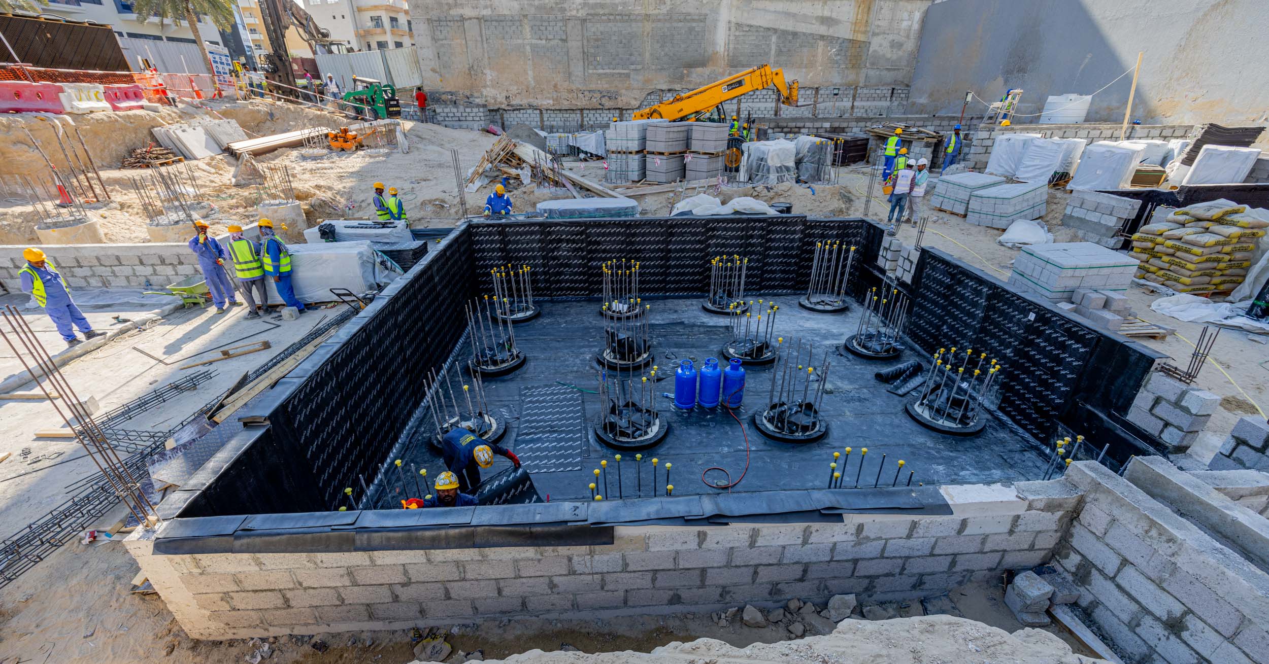 Pearl House By Imtiaz Construction site with workers, machinery, and a foundation pit featuring rebar and concrete blocks.